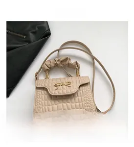 Detail of beige crocodile embossed crossbody bag with metal bow and pleated handle