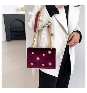 Detail of burgundy velvet crossbody bag with golden star studs and chain strap