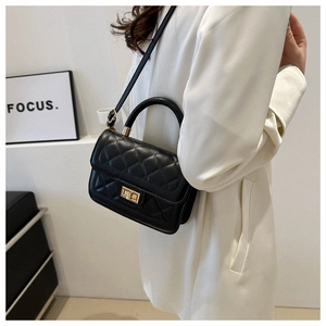Sac bandoulière noir matelassé avec fermoir doré porté par un mannequin en manteau blanc