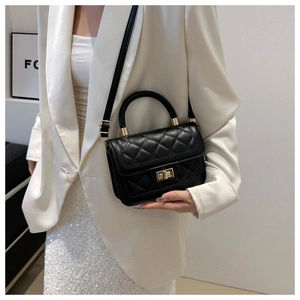 Détail du sac matelassé noir avec fermoir doré porté sur un tailleur blanc