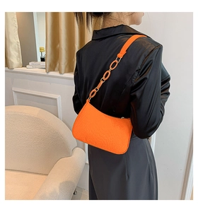 Close-up of bright orange croc-embossed baguette bag with resin chain strap detail