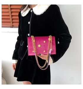 Detail of fuchsia velvet small square bag with golden sunburst hardware and chain