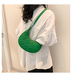 Détail du sac croissant vert avec relief de trèfle sur une chemise blanche