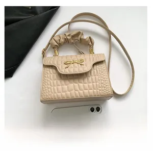 Close-up of beige crocodile pattern bag featuring a golden bow buckle and pleated handle