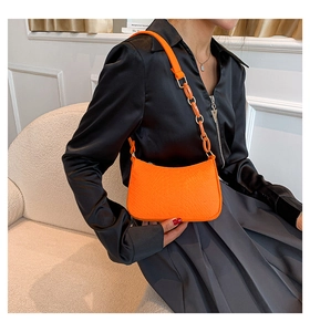 Orange croc-embossed underarm bag with resin chain strap shown on a model