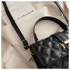 Detailed macro view of black quilted leather texture and gold twist-lock on handbag
