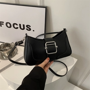 Sac baguette minimaliste en cuir noir avec boucle carrée argentée sur un socle géométrique