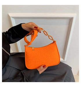 Detail of orange faux crocodile skin texture and thick decorative chain on crossbody bag