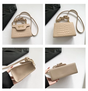 Detail view of beige crocodile embossed bag with knotted handle and golden bow clasp
