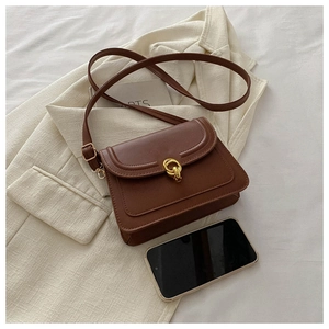 Close-up of brown vintage leather crossbody bag with gold buckle and smartphone for scale