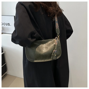Macro detail of dark green oil-wax leather pillow bag with floral strap on black coat