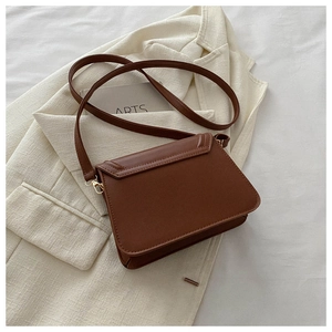 Close-up of brown faux leather crossbody bag with golden buckle on a beige blazer