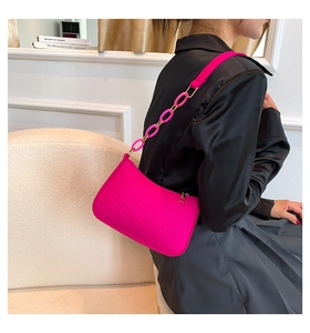 Detail of fuchsia crocodile pattern shoulder bag with golden chain strap on a model