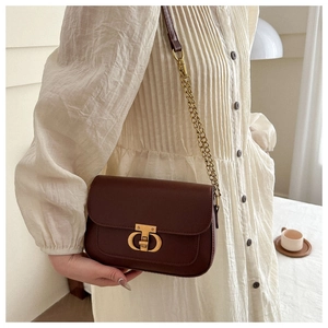 Gros plan du sac selle en cuir marron avec boucle CD dorée et bandoulière chaîne