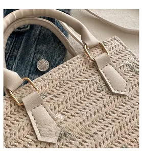 Detail of beige woven handbag featuring green floral embroidery and gold metal rings