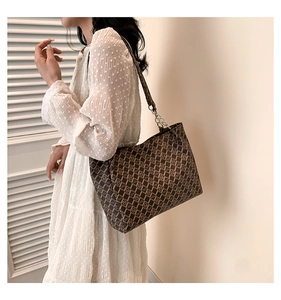 Detail view of large tote bag with classic pattern and metal chain strap on model