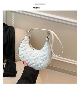 Detail of white crescent bag featuring embossed floral patterns and adjustable strap
