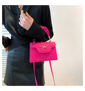 Close-up of rose red crocodile embossed handbag with gold bow and pleated handle