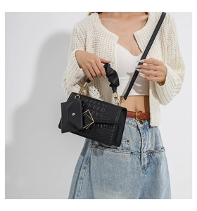 Detail of black crocodile texture bag with gold buckle and pleated fabric handle wrap