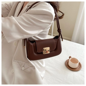 Close-up of brown leather underarm bag featuring a golden square buckle and knot strap detail
