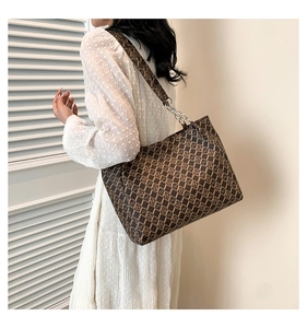 Detail of a brown tote bag with classic pattern, wide shoulder strap and silver chain links
