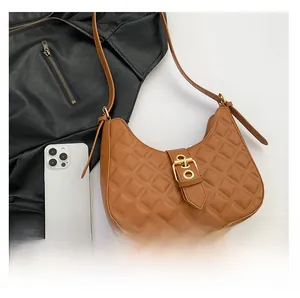Top view of brown quilted saddle bag with gold buckle and size comparison to phone