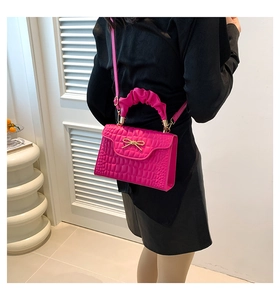 Detail of rose pink crocodile embossed handbag with golden bow and ruffled handle