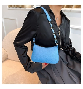 Close-up of sky blue faux leather shoulder bag with resin chain strap on sofa