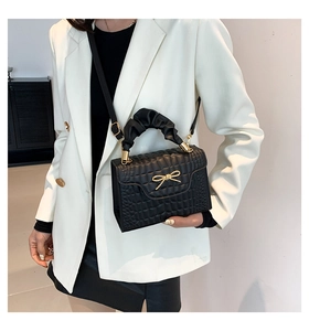 Detail of black faux leather mini bag with crocodile texture and gold bow chain