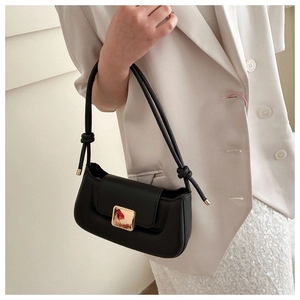 Detail of a black leather underarm bag with a gold square buckle and knotted strap