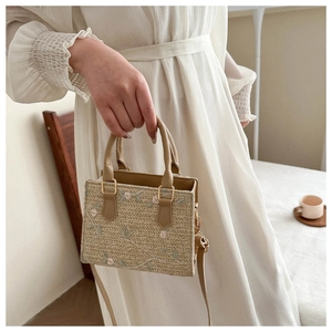 Detail of hand-woven straw bag featuring delicate floral embroidery and leather handles