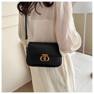 Sac à bandoulière chic en cuir noir avec fermoir doré en T sur une robe blanche