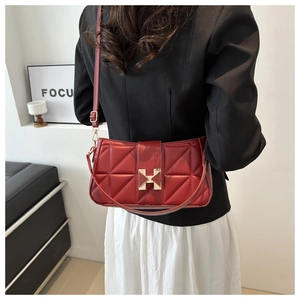 Reddish brown quilted crossbody bag with golden H buckle shown on model in black blazer