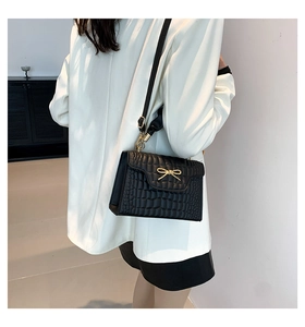 Detail of a black faux-crocodile shoulder bag with gold bow on a white suit jacket