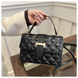 Detail of black quilted leather handbag featuring a golden rectangular metal clasp and handle