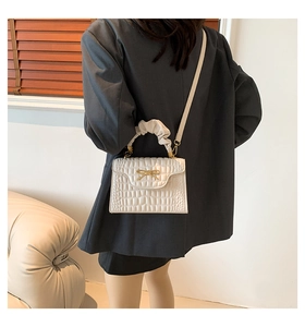 Detail of white crocodile pattern handbag with gold bow and beige gathered handle