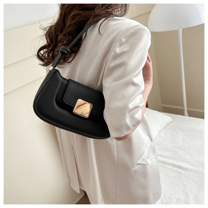 Detail of a black leather handbag with a gold square buckle worn with a beige blazer