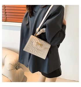 Close-up of cream crocodile pattern bag with a decorative gold bow buckle detail