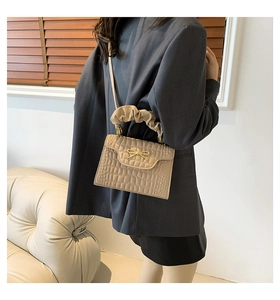 Detail of beige crocodile pattern handbag with pleated handle and golden bow accent