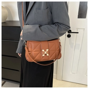 Detailed view of brown quilted handbag featuring geometric patterns and a golden X metal buckle