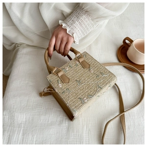 Close-up of woven straw bag with floral embroidery and vegan leather handles