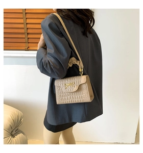 Detail of beige faux crocodile shoulder bag with golden bow and ruffled handle
