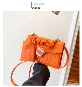Detail of orange crocodile pattern handbag with cloud handle and mini charm bag