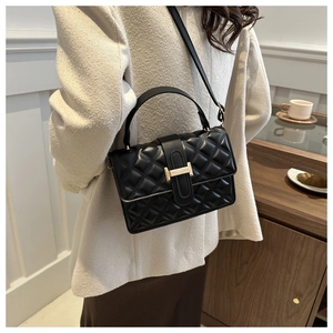 Detail of black quilted leather crossbody bag with gold H clasp on a minimal background