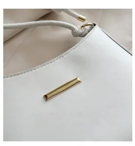 Detail of white leather bag featuring gold rectangular hardware and smooth shoulder strap