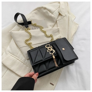 Detail of black quilted shoulder bag with gold hardware and tassel on cream blazer