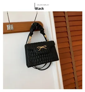 Detail of black crocodile texture handbag with golden bow and pleated handle