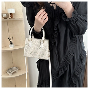 Detailed close-up of woven cream straw bag with elegant green floral leaf embroidery