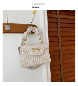 Detail of white crocodile pattern handbag with elegant gold bow and pleated handle