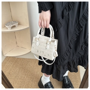 Detail of floral embroidery on cream woven handbag with leather handle and gold hardware